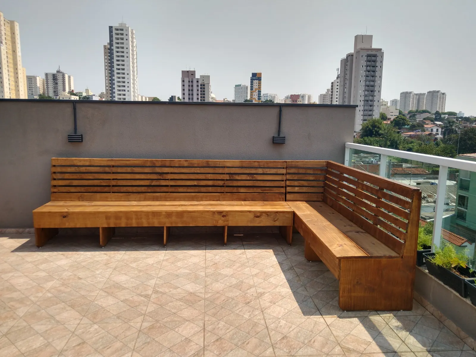 Banco de madeira em L com encosto em terraço com vista para prédios
