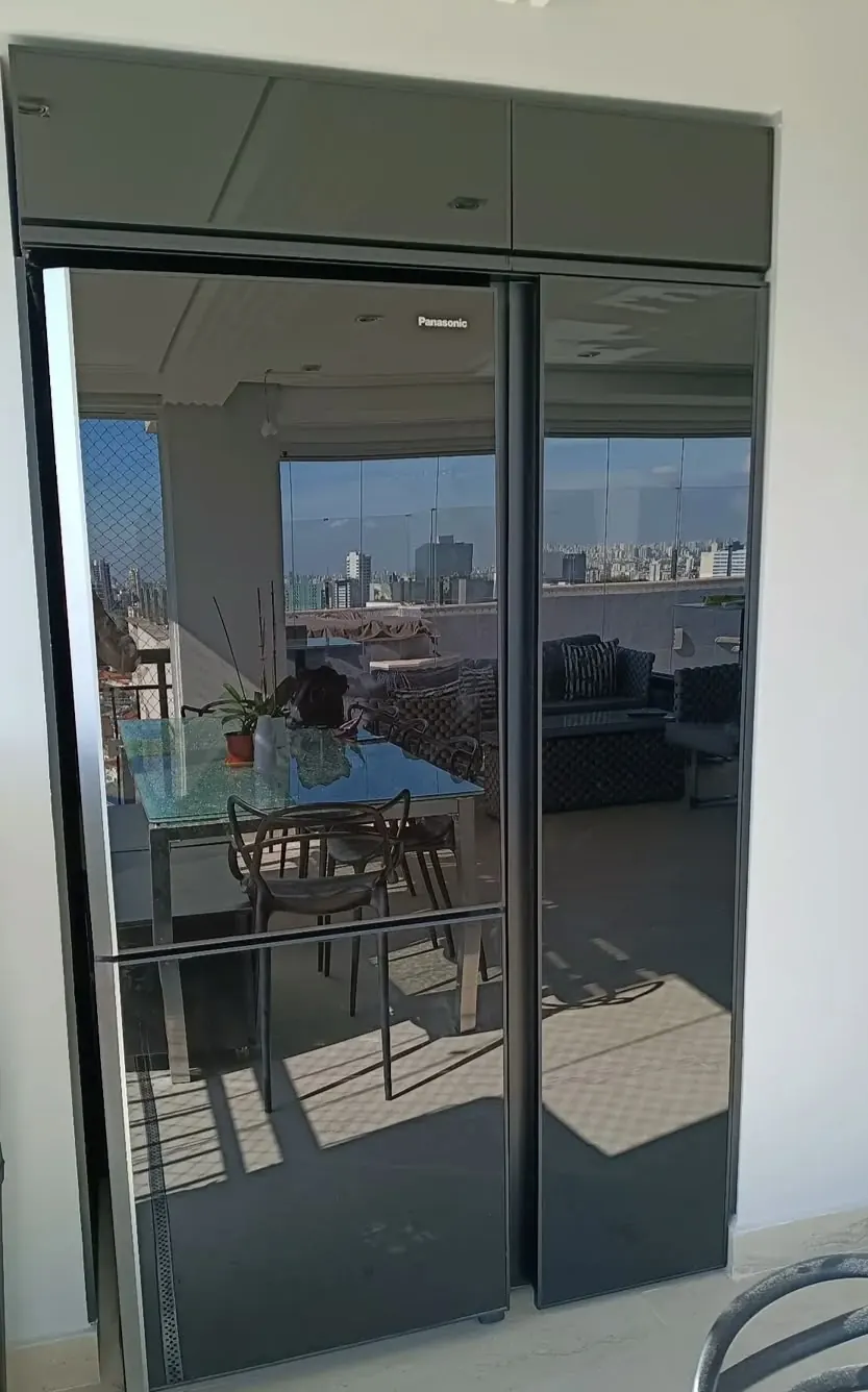 Porta alta de vidro com moldura escura, com a sala e a janela ao fundo